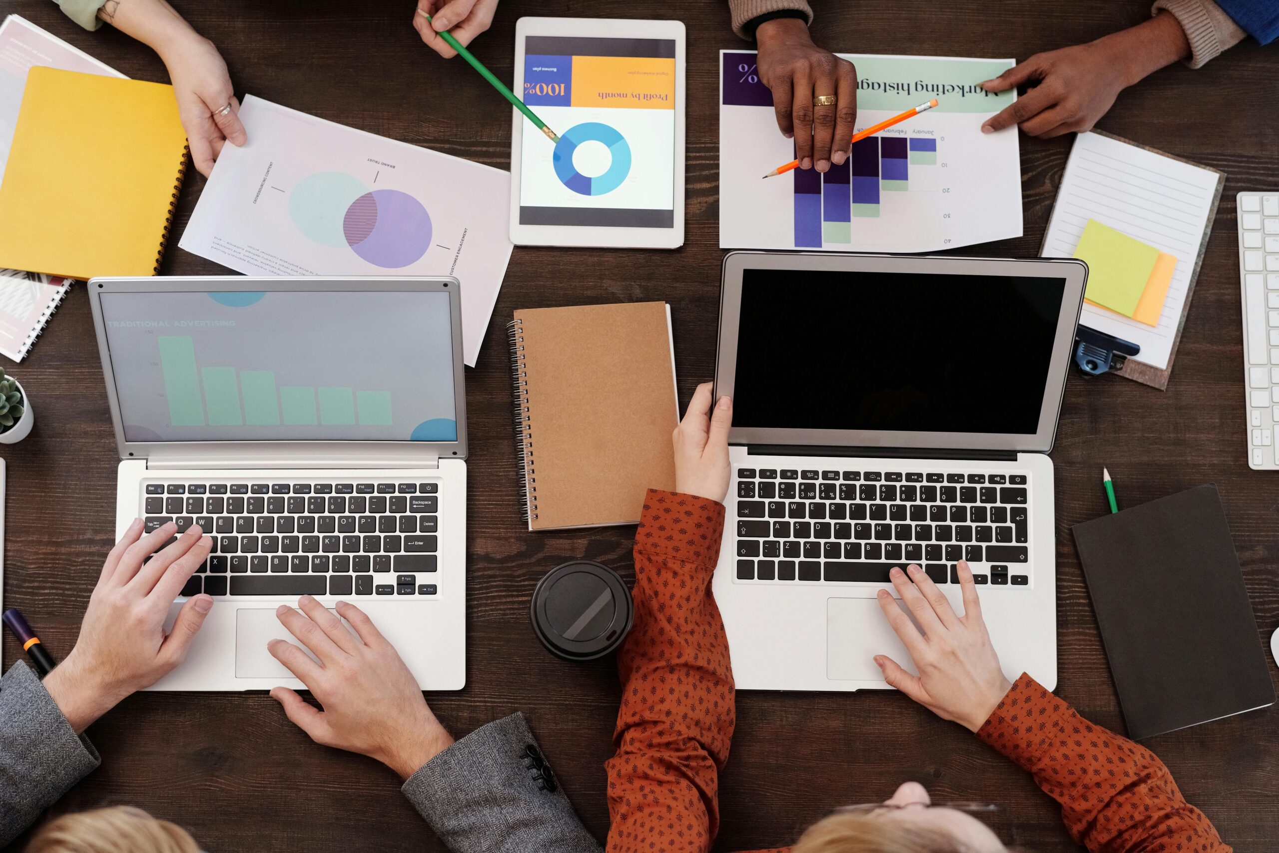 Four peoples hands and laptops on a work desk